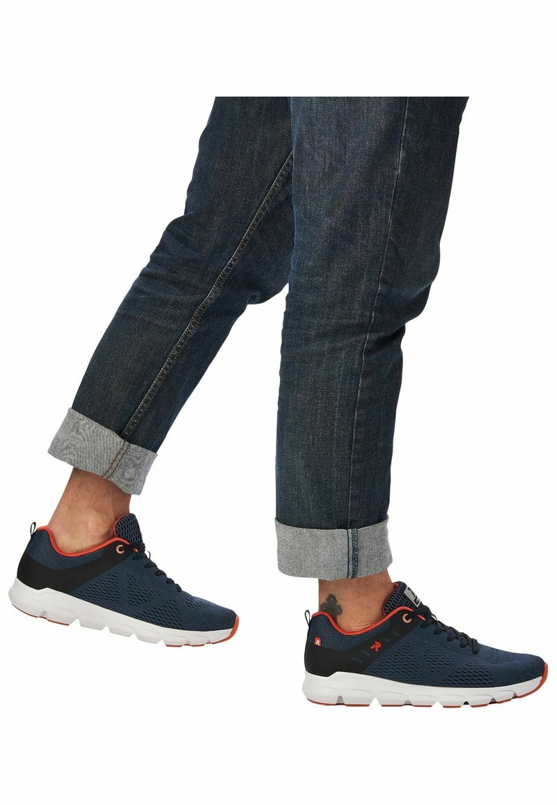 Athletic shoes in navy blue with black accents, mesh upper, white sole, and orange detailing; paired with rolled denim jeans.