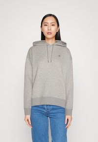 Hall halliga sweatshirti, millel on esikott, nöörid ja soonikkoes. Valmistatud pehmest kangast, millel on minimaalne tikandlogoga rinnal.