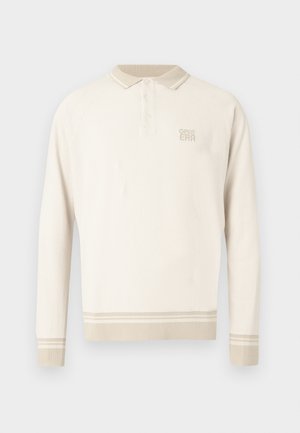 Polo de manga larga de color beige con tejido de punto texturizado, cuello con botones y rayas en el dobladillo y los puños. Presenta una sutil marca en el pecho.