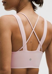 Różowy stanik sportowy z krzyżującymi się ramiączkami i szerokim pasem. Gładka faktura, minimalne logo z tyłu, zaprojektowany z myślą o komforcie i wsparciu.