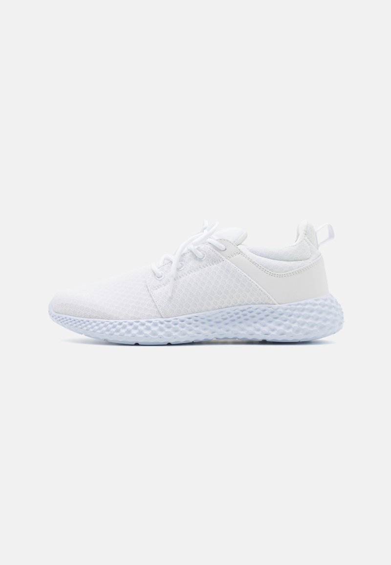 Chaussure de sport blanche avec tige en maille, design incurvé, fermeture à lacets et semelle en caoutchouc texturée et légère.