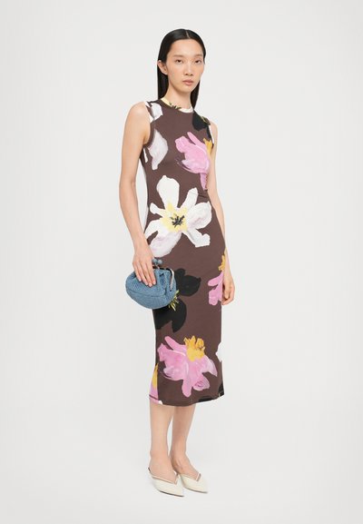 Sleeveless floral midi dress in brown, featuring pink, white, and yellow flowers. Model holds a blue woven clutch and wears white pointed flats.