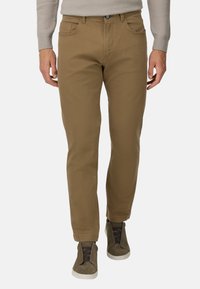 Pantalones de algodón marrón con un diseño de pierna recta, que cuentan con bolsillos frontales y un cierre de botón. Combinados con zapatillas altas grises.