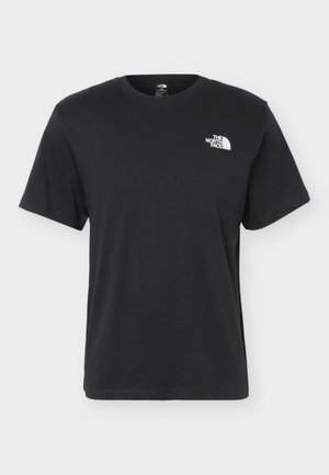 Joven con cabello rubio que lleva una camiseta negra de The North Face con gráficos de montañas y escaladores con el texto "Athlete Tested" y "Expedition Proven".