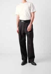 Witte katoenen t-shirt met korte mouwen, gecombineerd met zwarte, wijde broek en zwarte leren schoenen, compleet met een zwarte riem.