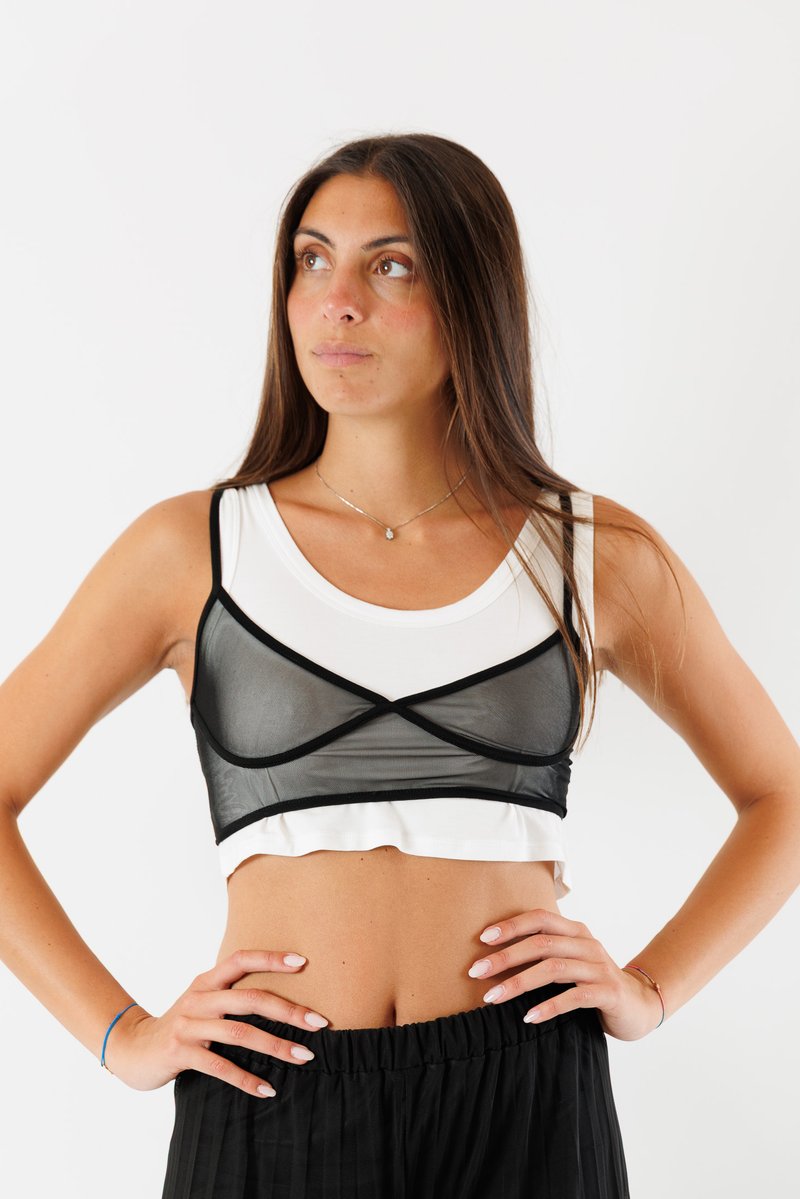 Top corto nero trasparente sovrapposto a un tank top bianco aderente, con finiture nere a contrasto e un design a spalline incrociate. Indossato con pantaloni a vita alta.