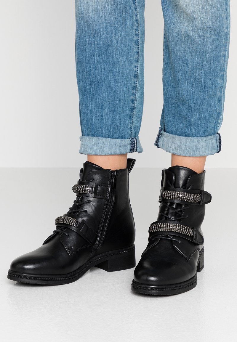 Botas de cuero negro hasta el tobillo con una textura suave, que cuentan con dos correas decorativas adornadas con tachuelas plateadas y un tacón bajo tipo bloque.
