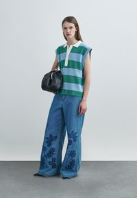 Haut sans manches tricoté à rayures vertes et bleues avec un col, associé à un pantalon en denim à jambes larges orné de broderies florales et un sac noir.
