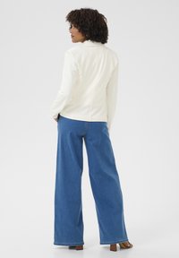 Veste blanche ajustée avec une coupe slim, dotée d'un col cranté, associée à un pantalon en denim bleu à jambes larges. Tissu lisse et lignes épurées.