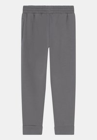 Sive trenirke s rebrastim elastičnim pojasom, bočnim džepovima i suženim manžetama na gležnjevima, izrađene od mekog, glatkog materijala.