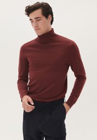 Pulover cu guler înalt de culoare vișinie, într-o croială slim, fabricat dintr-un material tricotat moale, cu mâneci lungi și textură netedă, asortat cu pantaloni închiși la culoare.