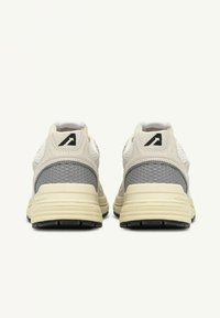 Une paire de chaussures de sport beige et grises montrées de dos, avec des panneaux de talon texturés et un logo noir sur l'onglet de talon.