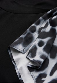 Svart topp med en slät textur, med en flödig ärm i grå och svart djurmönster. Ärmen har ett mjukt och lätt tyg.