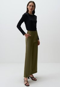 Czarny prążkowany top z długim rękawem w połączeniu z oliwkowymi spodniami o wysokim stanie i szerokich nogawkach, charakteryzującymi się gładką satynową fakturą i bocznymi kieszeniami.