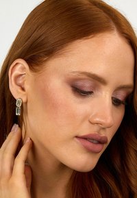 Boucles d'oreilles pendantes avec une pierre rectangulaire transparente suspendue à un monture dorée, ornées d'un accent ovale texturé au-dessus.