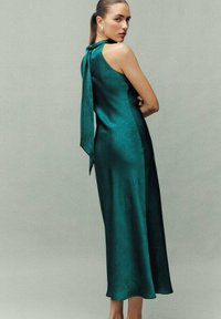 Vestido de satén verde con un corsé ajustado, espalda baja y detalle de lazo en el cuello. Falda fluida de longitud media con una textura sutil.