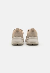 Beige nubukist sneakers tekstureeritud viimistlusega, ümar kuju ja paks valge tald; sisaldab kandmistõmblust ja minimalistlikku disaini.