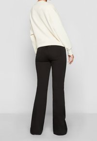 Suéter crema, jeans negros acampanados. Los jeans cuentan con una cinturilla estándar y bolsillos traseros, ofreciendo un estilo ajustado de caderas a rodillas.