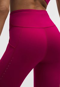 Dopasowane legginsy z wysokim stanem w jasnoróżowym kolorze o gładkiej fakturze, z bocznymi kieszeniami i dekoracyjnymi metalowymi kropkami wzdłuż nogawki.
