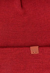 Czerwona, wełniana czapka beanie z fakturowaną powierzchnią i złożonym mankietem. Posiada małą, prostokątną skórzaną metkę z wytłoczonym logo.