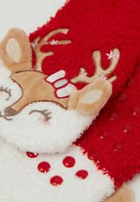 Červené plyšové ponožky se sobím motivem, s jemnými texturami, vyšívanými detaily a vystouplými červenými puntíky na bílém podkladu.