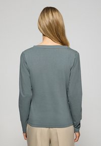 Långärmad skjorta i skiffergrå, med en vid halsringning och mjukt tyg. Tydlig sömnad och jämn textur är synlig.