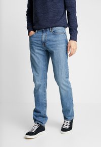 Jeans de denim azul claro con corte recto, que cuentan con un clásico diseño de cinco bolsillos y sutiles detalles de desgaste, combinados con zapatillas negras.