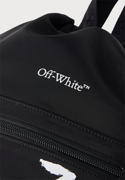 Κοντινό πλάνο μαύρου σακιδίου πλάτης Off-White που δείχνει λευκό λογότυπο και μαύρο φερμουάρ σε ομαλό υφασμάτινο υλικό.