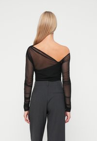 Top lungo a maniche trasparenti nera con design off-shoulder e dettagli arricciati, abbinato a pantaloni grigi a vita alta. Texture liscia, forma aderente.