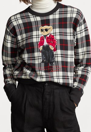 Sort, hvid og rød ternet sweater med grafik af en bjørn iført solbriller, rød jakke, hvid skjorte og sorte bukser.