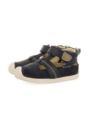 Zapatos de cuero y tela en color navy con tiras de velcro, acentos en color beige en contraste y suela texturizada. Presentan puntera redondeada y diseño abierto.