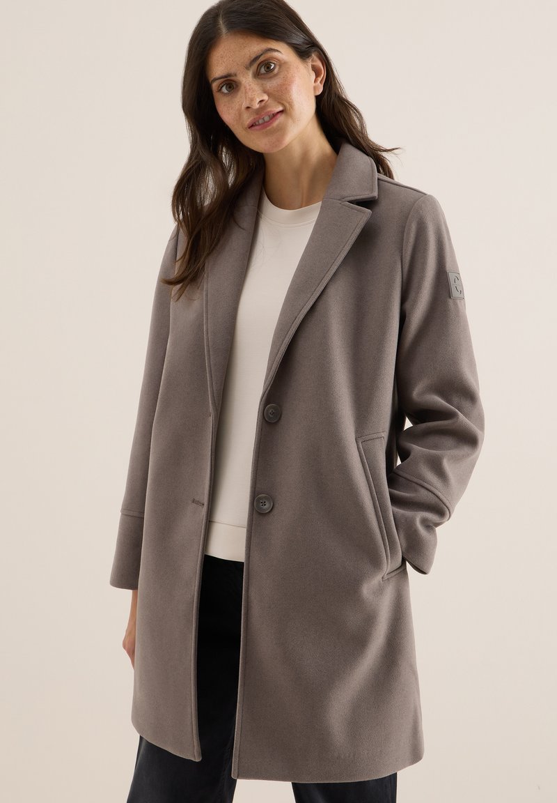 Manteau en mélange de laine gris au design ajusté, avec de grands revers, deux boutons et des poches latérales. Présente un léger logo brodé sur la manche.