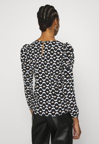 Černobílé tričko s dlouhým rukávem a geometrickým vzorem. Disponuje nabíranými rameny a detaily ve tvaru klíčové dírky na zadní straně. Hladká textura látky.