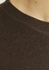 Maglione marrone a maglia con collo rotondo a coste e tessuto testurizzato. La superficie presenta un motivo sottile con variazioni di spessore.