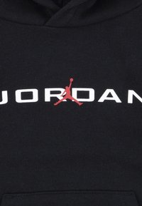 Fekete kapucnis felső, középen nagy, fehér "JORDAN" logóval és piros Jumpman siluettel, puha, textúrált anyagból készült.