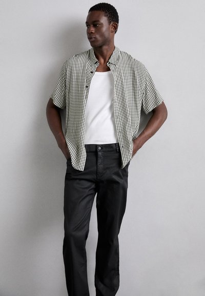 Chemise à manches courtes, à carreaux noir et blanc, sur un débardeur blanc, associée à un pantalon noir. Tissu doux, coupe décontractée.