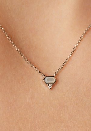 Collier en chaîne en argent avec un pendentif hexagonal orné d'une pierre blanche et d'un petit cristal en accent au bas.
