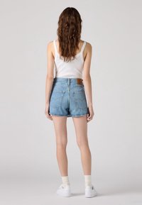 Ljusblå denimshorts med fransig fåll, bakfickor och en brun läderlapp. Kommer med en vit linne och vita sneakers.