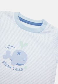 Un body de bebé a rayas azul claro con un gráfico de ballena azul y detalles en verde. Presenta cierres a presión en el hombro y una textura de tela suave.