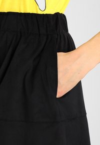 Svart kjol med gatherad midja, försedd med en sidoficka. Tyget är slätt med en subtil textur. Midjebandet är elastiskt för komfort.