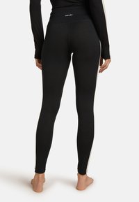Leggings negros con cintura alta, tela suave y ajuste ceñido. Presentan acentos laterales en contraste y un logo en la parte posterior de la cintura.