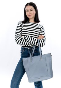 Tote bag bleu clair en cuir texturé, doté de deux anses robustes et d'un matériel minimal. Modèle portant un haut rayé et un jean.