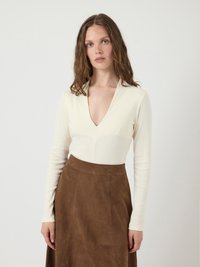 Valkoinen pitkähihainen paita syvällä V-kaula-aukolla, yhdistettynä ruskeaan mokkanahkahameeseen. Paidassa on ribbitekstuuri ja slim fit -malli.