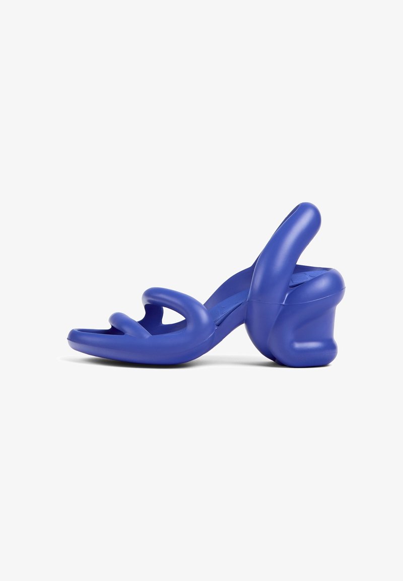 Sandale bleue moulée avec un talon épais, présentant un design à bride enveloppante et une surface texturée. Forme sculpturale unique soulignant un style contemporain.