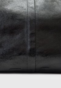 Borsa in pelle nera con una superficie testurizzata, caratterizzata da cuciture a vista e un marchio impresso. Finitura liscia con elementi di design minimalista.