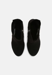 Bottes de cheville en daim noir avec une texture lisse, présentant une fermeture éclair sur le côté et un design à bout arrondi. Sans ornements ni motifs visibles.