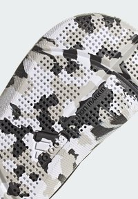 Suola della scarpa con un motivo camouflage in nero, bianco e grigio, dotata di perforazioni. Visibili dettagli di marchio e gomma non-marking.