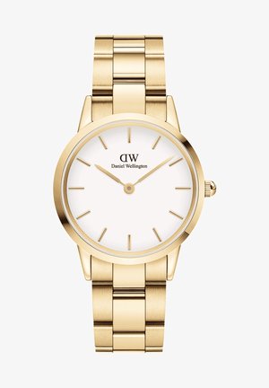 Kuldtooni randme kell ümmarguse korpuse, valge kelladiali, õhukeste tunni markerite ja metallkettide rihmaga. Omab minimalistlikku disaini.