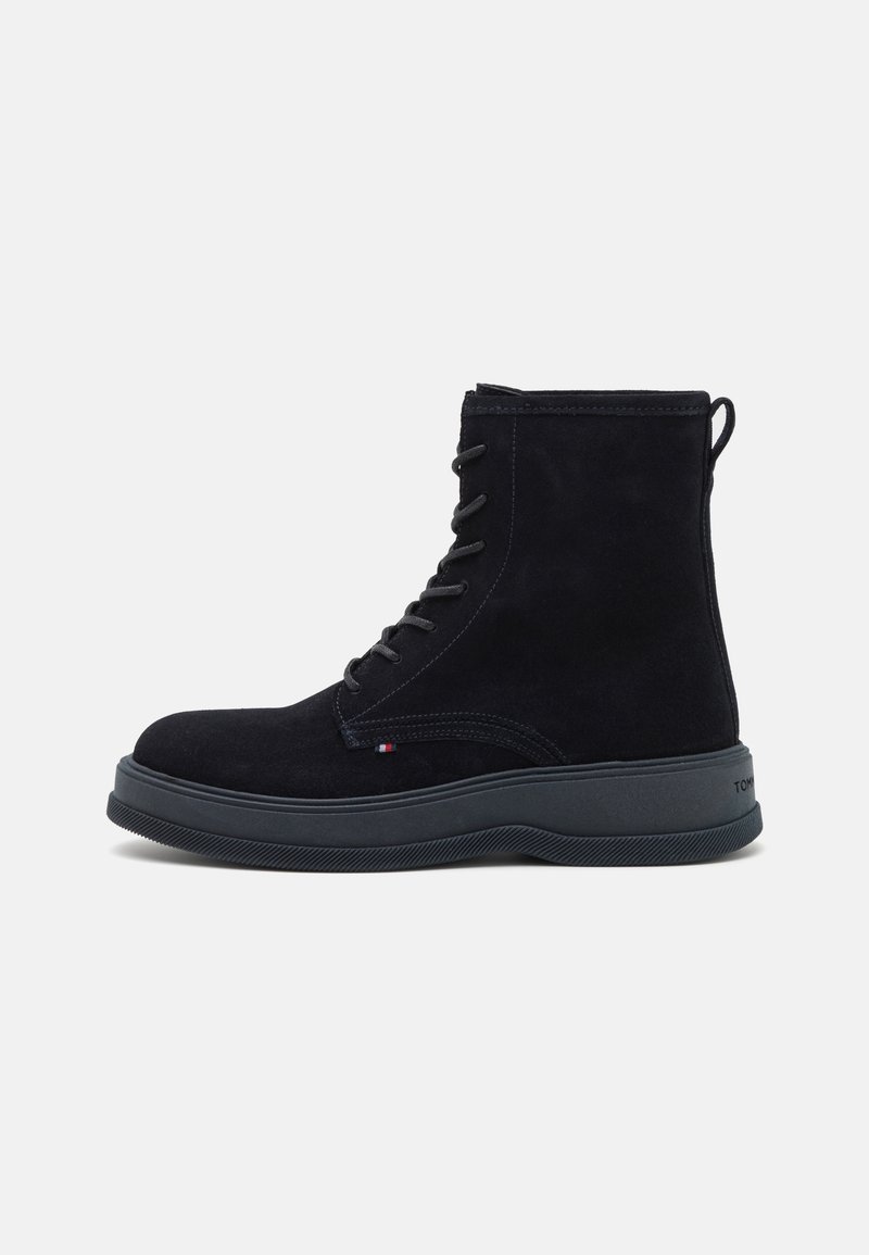 Botas de ante negras hasta el tobillo con un acabado texturizado, que cuentan con cordones, una lengüeta en el talón y una suela de goma contrastante. Diseño simple y funcional.