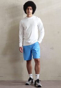 Valge pika varrukaga särk, helesinised lühikesed püksid Nike logo ja mustad spordijalatsid. Sile kangas ja mugav lõige.
